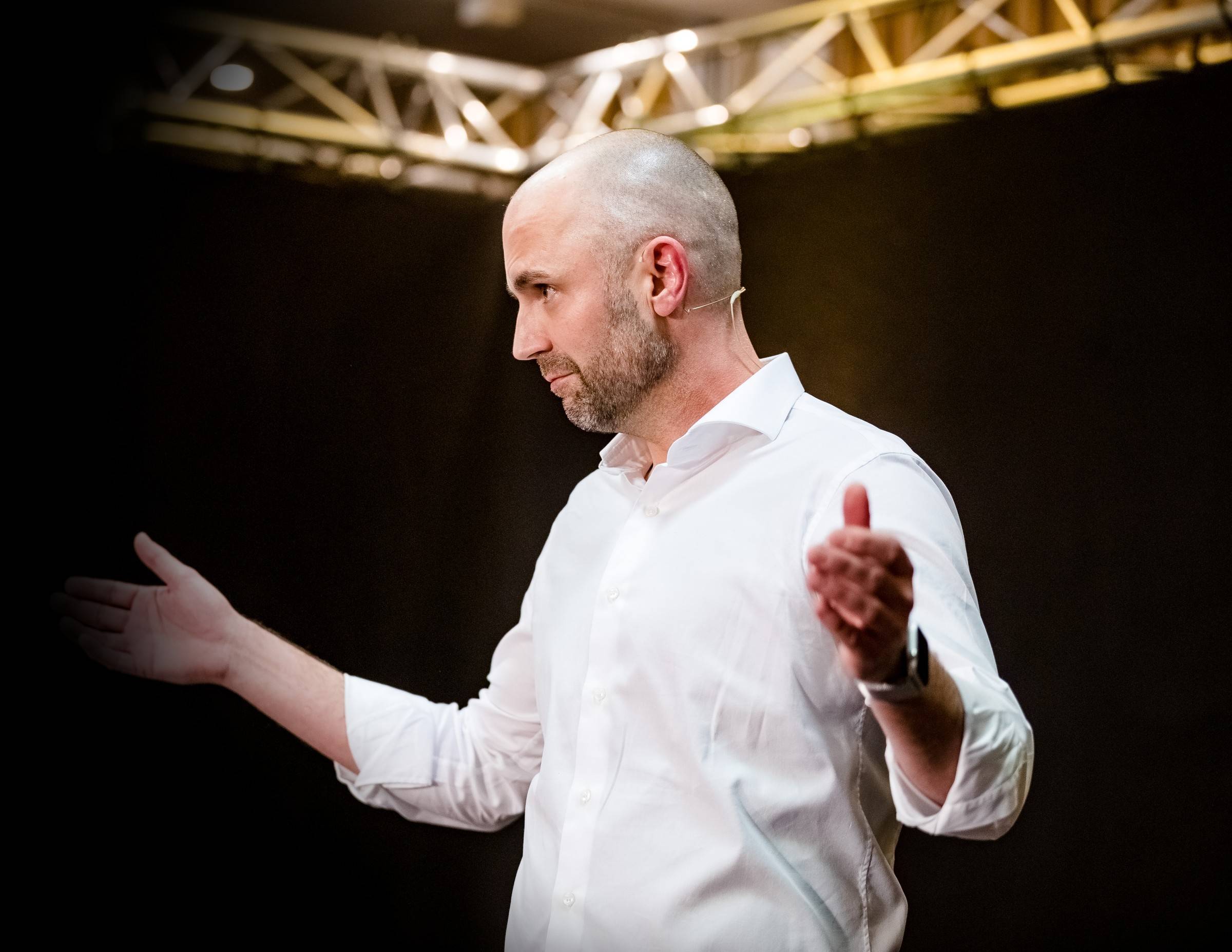 Dr. med. Niels Freitag auf der Bühne im weißen Hemd, eine Hand zum Publikum geöffnet
